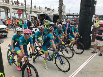 Eight cyclists of Team Sea to See in turquoise jerseys are mounted on four tandem bicycles at the start of the Race Across America in Oceanside California. Four of the cyclists are blind.